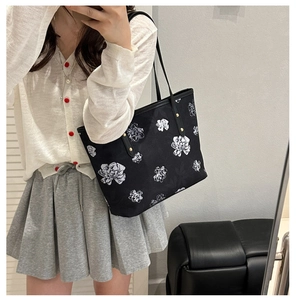 Detailed close-up of large black tote bag with white camellia flower prints and slim straps
