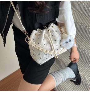 Details einer weißen Plissee-Beuteltasche mit Schleifen-Print und Plüsch-Monster-Anhänger