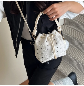 Detail der weißen Beuteltasche mit Schleifendesign, Flechtgriff und Plüschanhänger