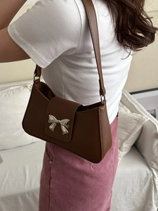 Sac à bandoulière en cuir marron avec boucle nœud argentée porté par un modèle