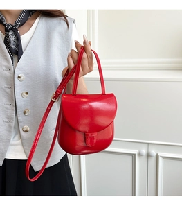 Detail of red glossy leather saddle bag featuring a polished finish and adjustable strap