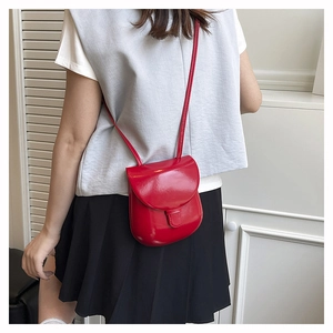 Detailed view of a red patent leather crossbody bag shown on a model in bright indoor light