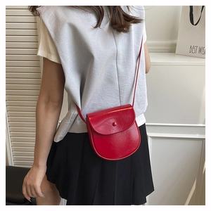 Close-up of bright red saddle bag in shiny patent leather with matching buckle detail