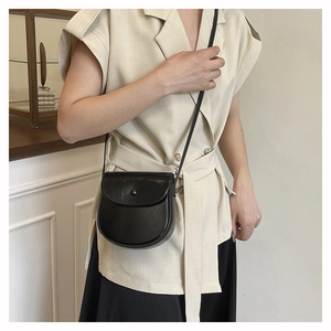 Close-up of a black semi-circular saddle bag worn by a model in a minimalist setting