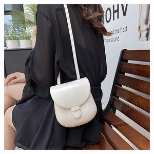 Model wearing a minimalist cream-colored leather saddle bag in a natural outdoor setting
