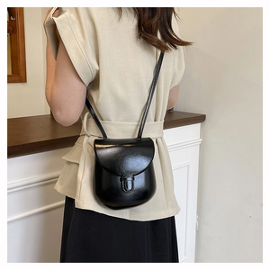 Close-up of a glossy black mini crossbody bag with a curved base and flap closure