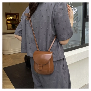 Brown vintage saddle bag worn by model in a warm cafe setting for a classic everyday look
