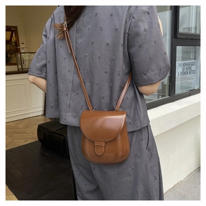 Brown faux leather saddle bag with adjustable strap worn on a grey pleated outfit
