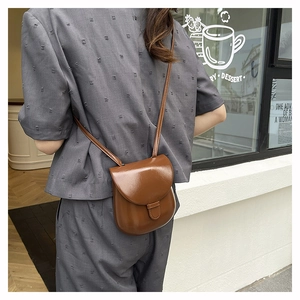 Detail of a brown vintage leather crossbody saddle bag with flap closure and buckle strap