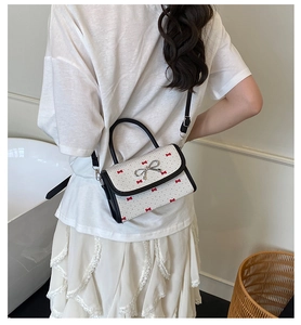 Modern white crossbody bag featuring red bow prints and a sleek black round handle