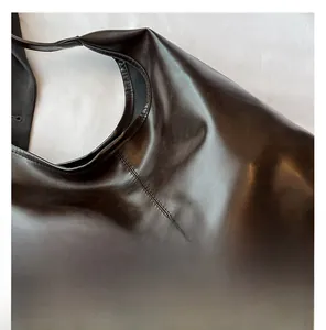 Detail der Seitennähte und des Riemenansatzes an der glänzenden dunklen Leder-Tote-Bag