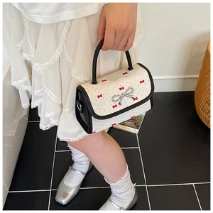 Detail of child hand holding a cream crossbody bag with red floral pattern and silver bow