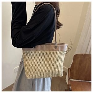 Detailed side view of a large woven straw tote bag with brown leather handles and silver buckles