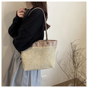 Detail of hand-woven straw tote bag featuring khaki leather trim and shoulder straps