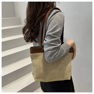 Detail view of a woven straw tote bag with brown leather handles and textured finish