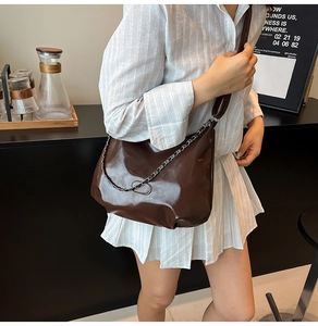 Detail of dark brown glossy patent leather crossbody bag with silver chain strap