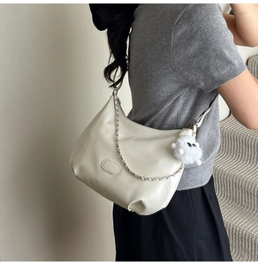 Detailed side view of beige PU leather half-moon shoulder bag with plush charm and chain