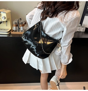 Detail of black glossy crescent crossbody bag with silver chain and white plush charm