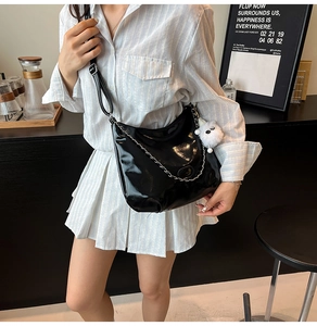 Close-up of black glossy crossbody bag with silver chain and white teddy bear charm
