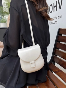 Minimalist white leather saddle crossbody bag shown on model in a modern outdoor setting