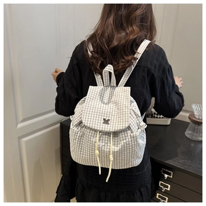 Detail showing checkered canvas backpack with drawstring closure and metal logo on a model