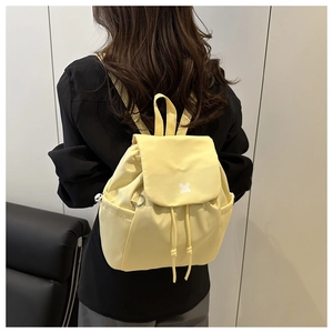 Detail of light yellow nylon backpack showing drawstring closure and flap with small icon