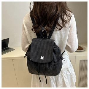 Close-up of black checkered canvas backpack featuring drawstring closure and silver metal buckle