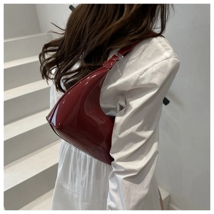 Detail view of a dark red patent leather underarm bag with glossy finish on white steps