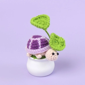 Detail of a handmade crochet turtle plant with purple shell and green leaves in a white vase