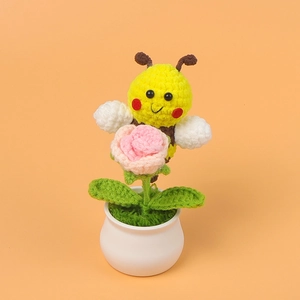 Detail of handmade crochet yellow bee holding a pink rose in a white ceramic vase