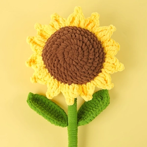Handmade crochet sunflower with soft yellow petals and green leaves on a yellow background