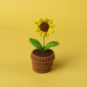 Close-up of a handmade crochet sunflower in a brown pot against a yellow background