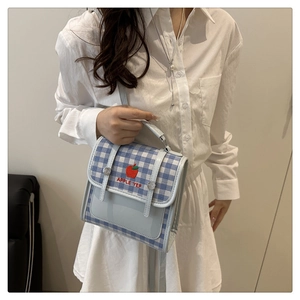 Detail of light blue plaid handbag featuring red apple embroidery and buckle closure