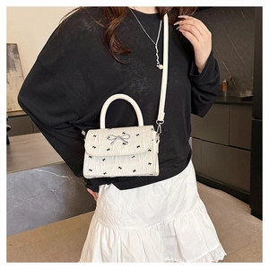 Détail d'un sac bandoulière blanc avec imprimés nœuds noirs et boucle argentée en forme de nœud