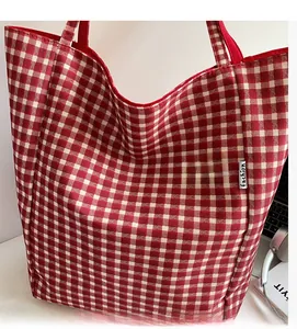 Detail shot of red plaid tote bag with fashion label on a desk with laptop