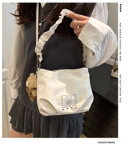 Detail of white cloud-shaped shoulder bag featuring pleated strap and plush teddy bear charm