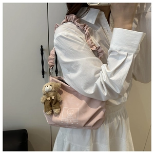 Detail of light pink crossbody bag featuring ruffled strap and cute teddy bear charm