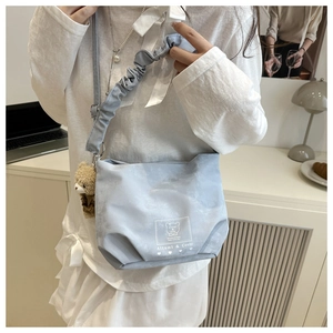 Detail of light blue shoulder bag featuring ruffled straps and cute bear doll pendant