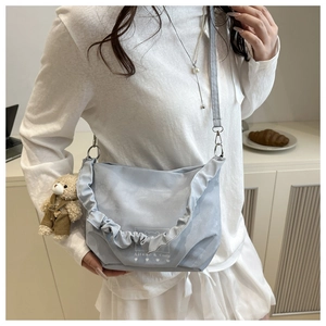 Detail of light blue crossbody bag featuring ruffled edges and a cute teddy bear charm