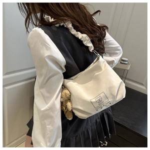 Detail of white shoulder bag featuring ruffled strap and a cute brown plush bear charm