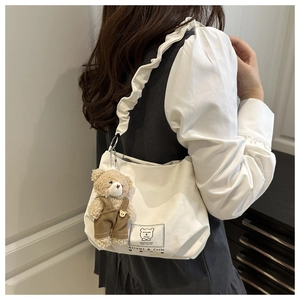 Detail of white canvas bag with ruffled shoulder strap and plush bear keychain accessory
