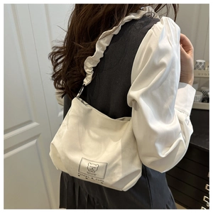 Close-up of off-white canvas bag featuring a pleated strap and cute bear patch detail