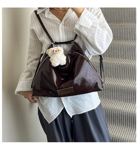 Detail of dark brown glossy tote bag with metal accents and cute plush bear charm
