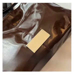 Detail shot of a brown patent leather tote bag with a silver metallic logo plate decoration