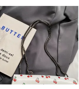 Détail de la bandoulière en chaîne foncée et de l'imprimé cerise sur le sac blanc