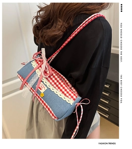 Detail of blue denim shoulder bag with red plaid bows and white lace trim detail