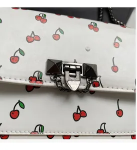Détail d'un sac en cuir blanc avec imprimés cerises et fermoir métallique brillant