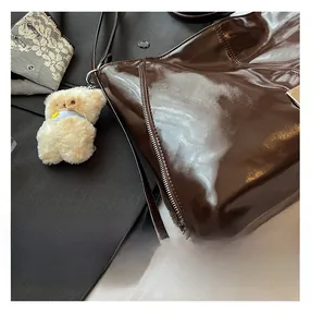 Detail of dark brown patent leather tote bag with metal zipper and plush bear charm
