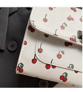 Gros plan d'un sac en cuir blanc avec imprimé cerises et fermoir métallique carré chic