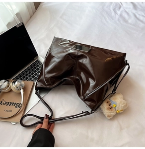 Detail of dark brown patent leather tote with silver hardware and plush bear charm